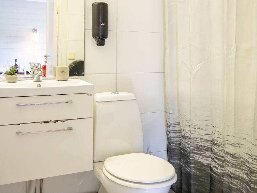 Un baño con un lavamanos blanco, un espejo, un inodoro y una cortina de ducha.