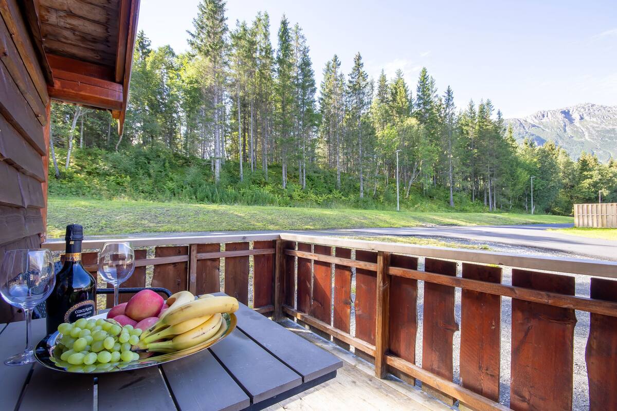 Una terraza de madera con una mesa dispuesta para una comida, que incluye un plato de fruta y dos copas de vino.