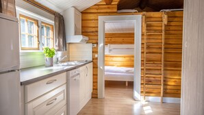 A compact kitchen with wooden walls, a built-in dishwasher, and a window with curtains. - Topcamp Mosjøen - Helgeland (Vefsn)