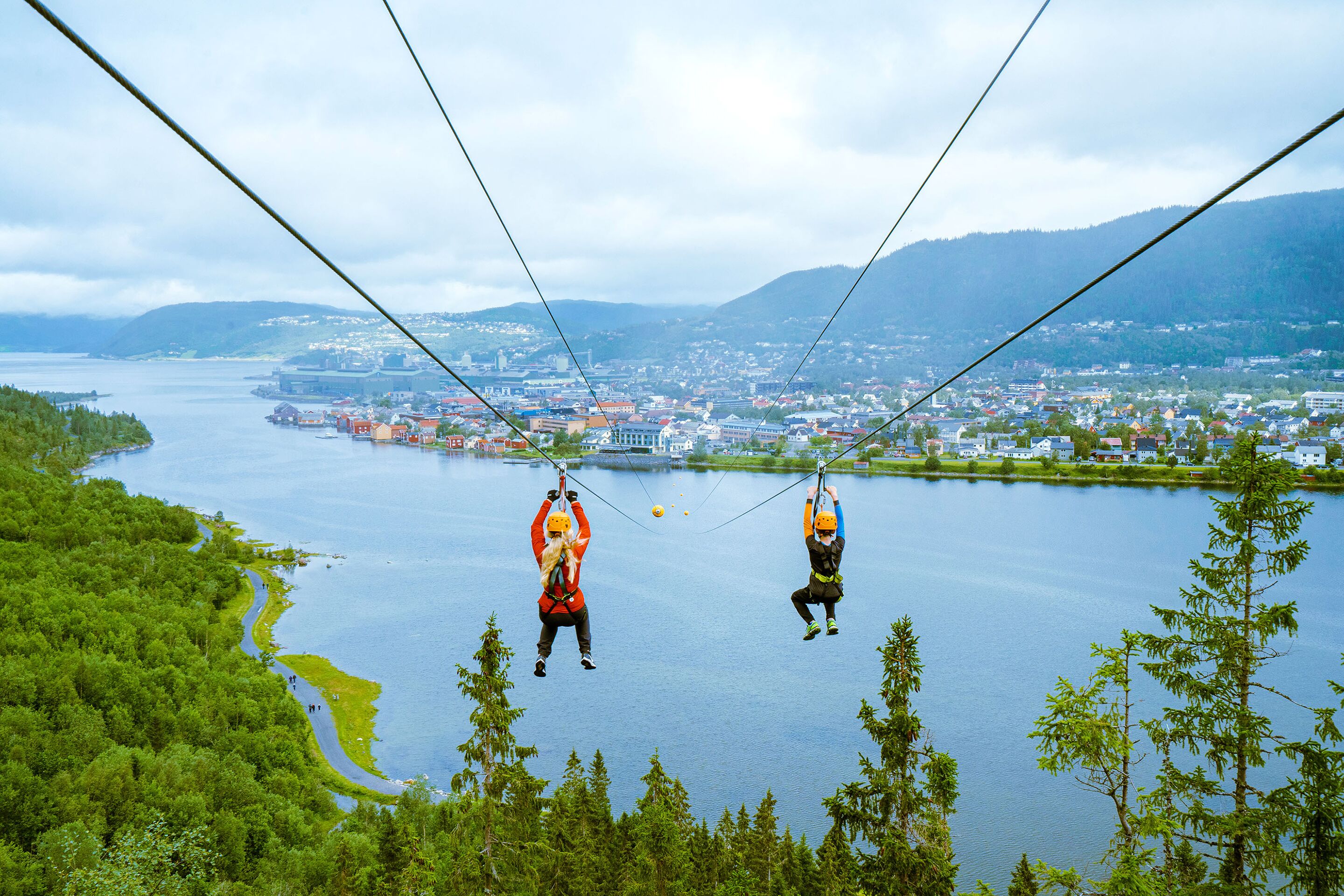 Dos personas hacen bungee jumping sobre un lago, con una ciudad al fondo.