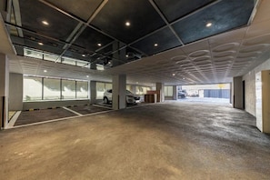 An indoor parking area with concrete flooring, ceiling lights, and large windows on one side. - HOTELIUM (Cheonan)