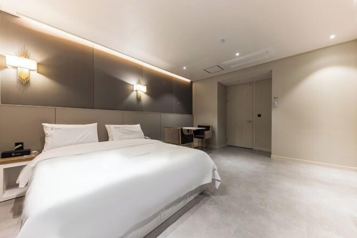 A modern hotel room with a large bed, bedside tables, a desk, and a walk-in closet.