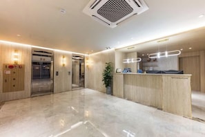 A hotel reception area with a marble floor, wooden reception desk, and two elevators. - HOTELIUM (Cheonan)