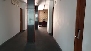 A hallway with a carpeted floor, a wooden door on the right, and a red chair in the distance. - Wir Hotel (Jakarta)
