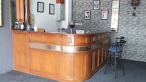 A reception area with a wooden counter, a cash register, and framed photographs on the wall. - Wir Hotel (Jakarta)