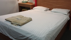 A neatly made bed with a folded towel and a bottle of water on the nightstand. - Wir Hotel (Jakarta)