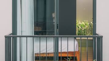A balcony with a bed, a window with curtains, and a plant.