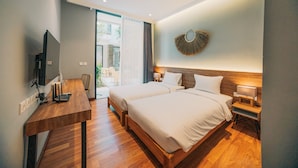 A modern hotel room with two beds, a wooden desk, a TV, and a balcony with plants. - Bestah Coliving (Denpasar)