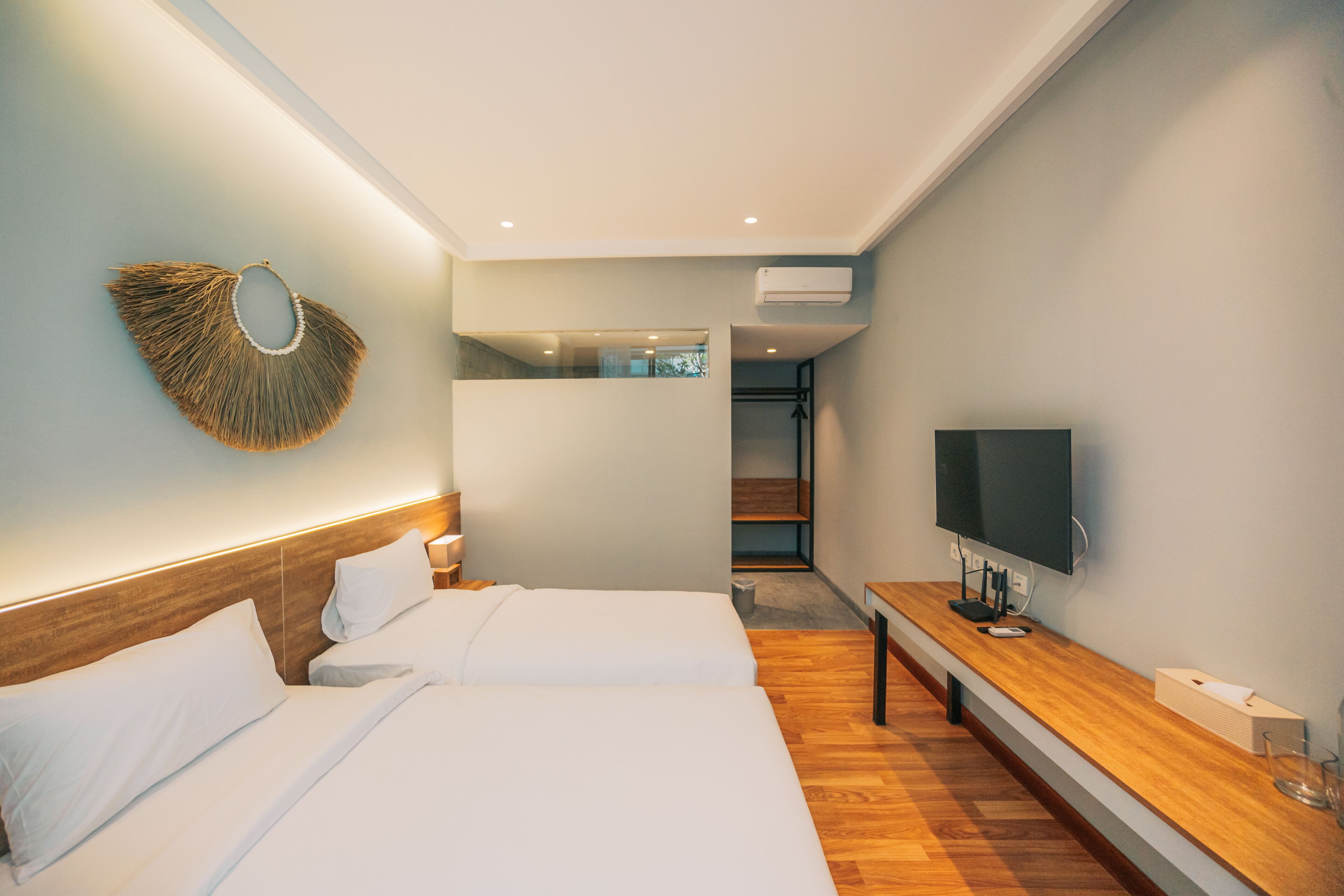 A modern hotel room with two beds, a wooden bedside table, a flat-screen TV, and a wall-mounted decorative item.