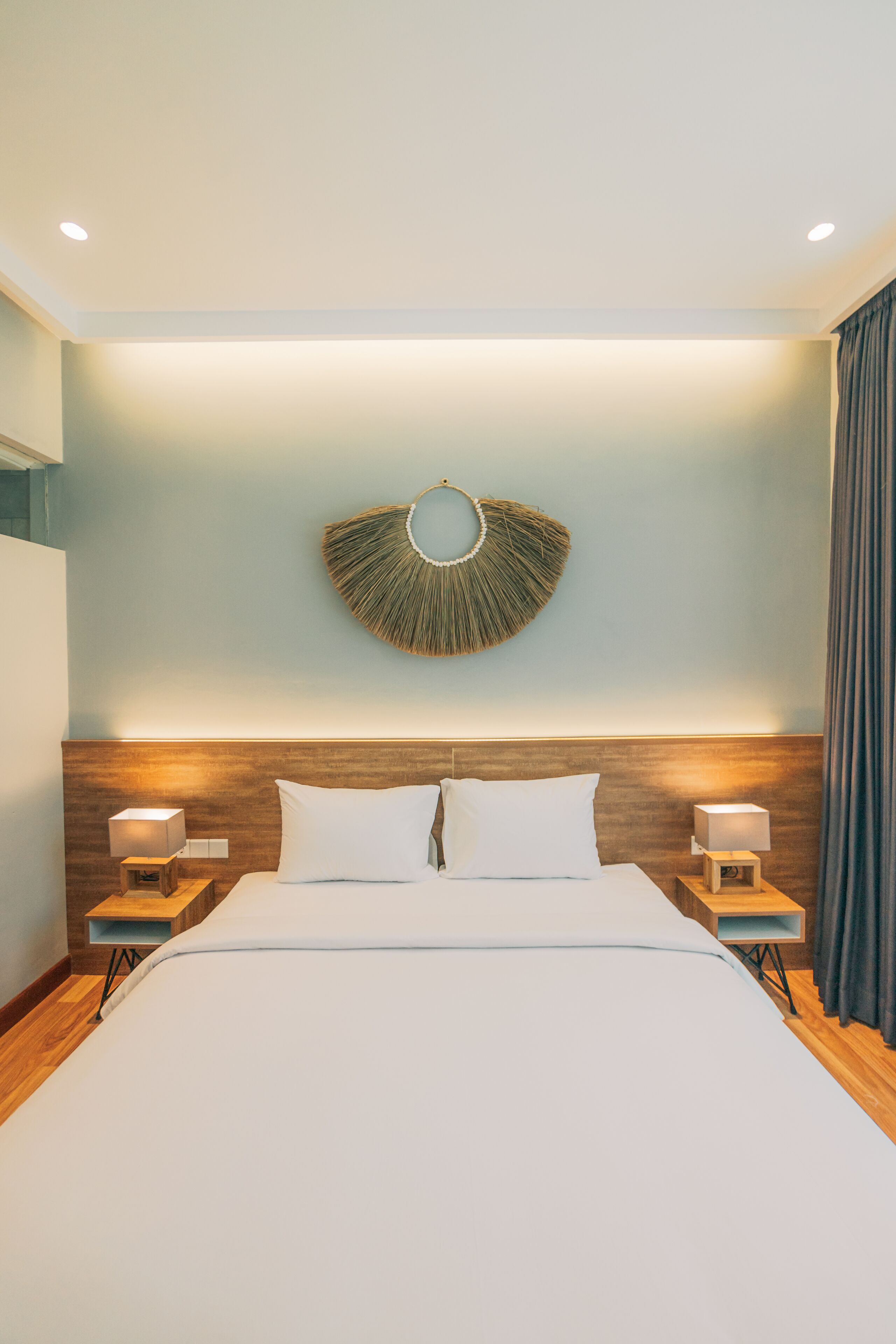 Una habitación de hotel moderna con una cama grande, cabecera de madera, dos mesitas de noche con lámparas y un adorno en la pared.