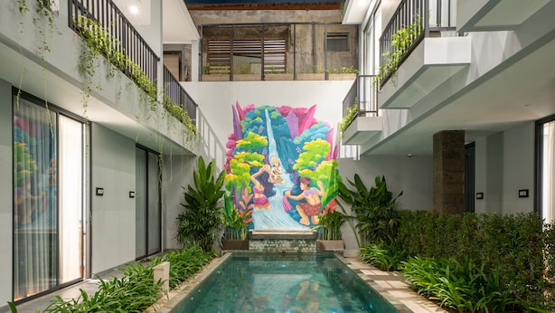 A modern hotel with a central swimming pool, surrounded by balconies with plants, and a mural on the wall. - Bestah Coliving (Denpasar)