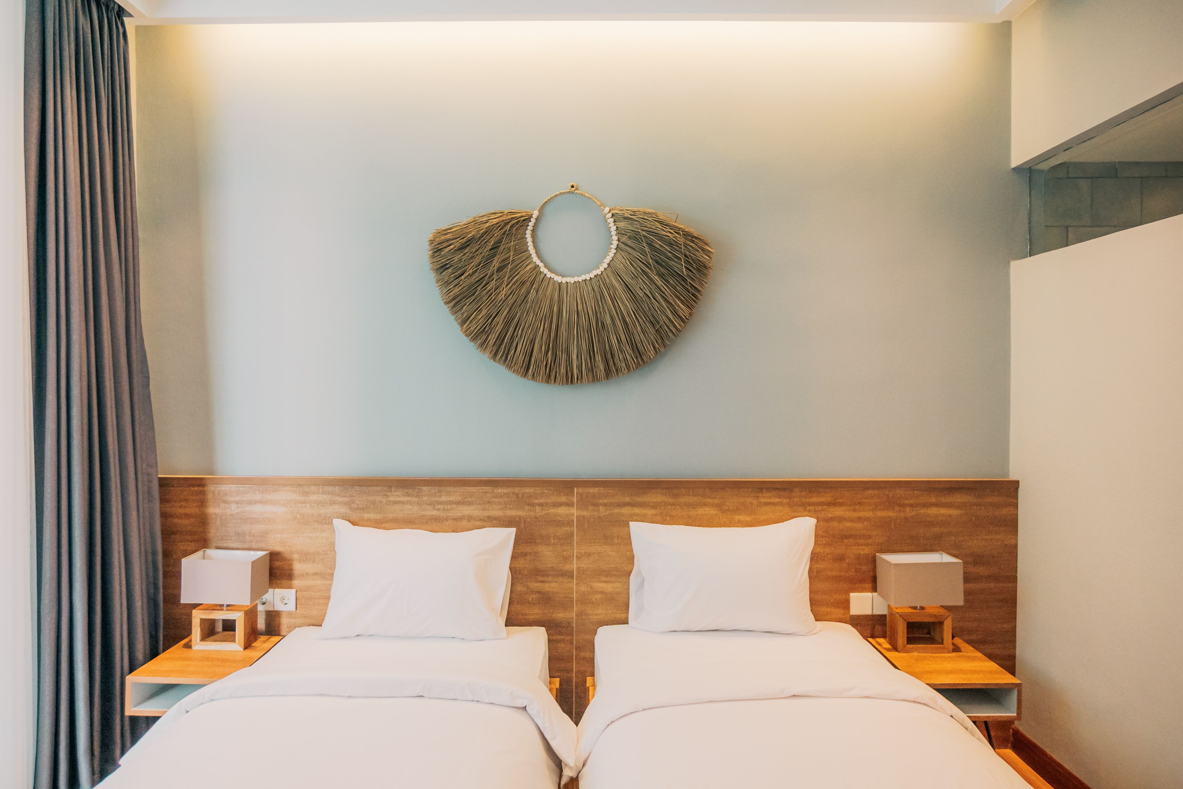 A hotel room with two beds, a wooden headboard, bedside lamps, and a wall-mounted decorative piece.