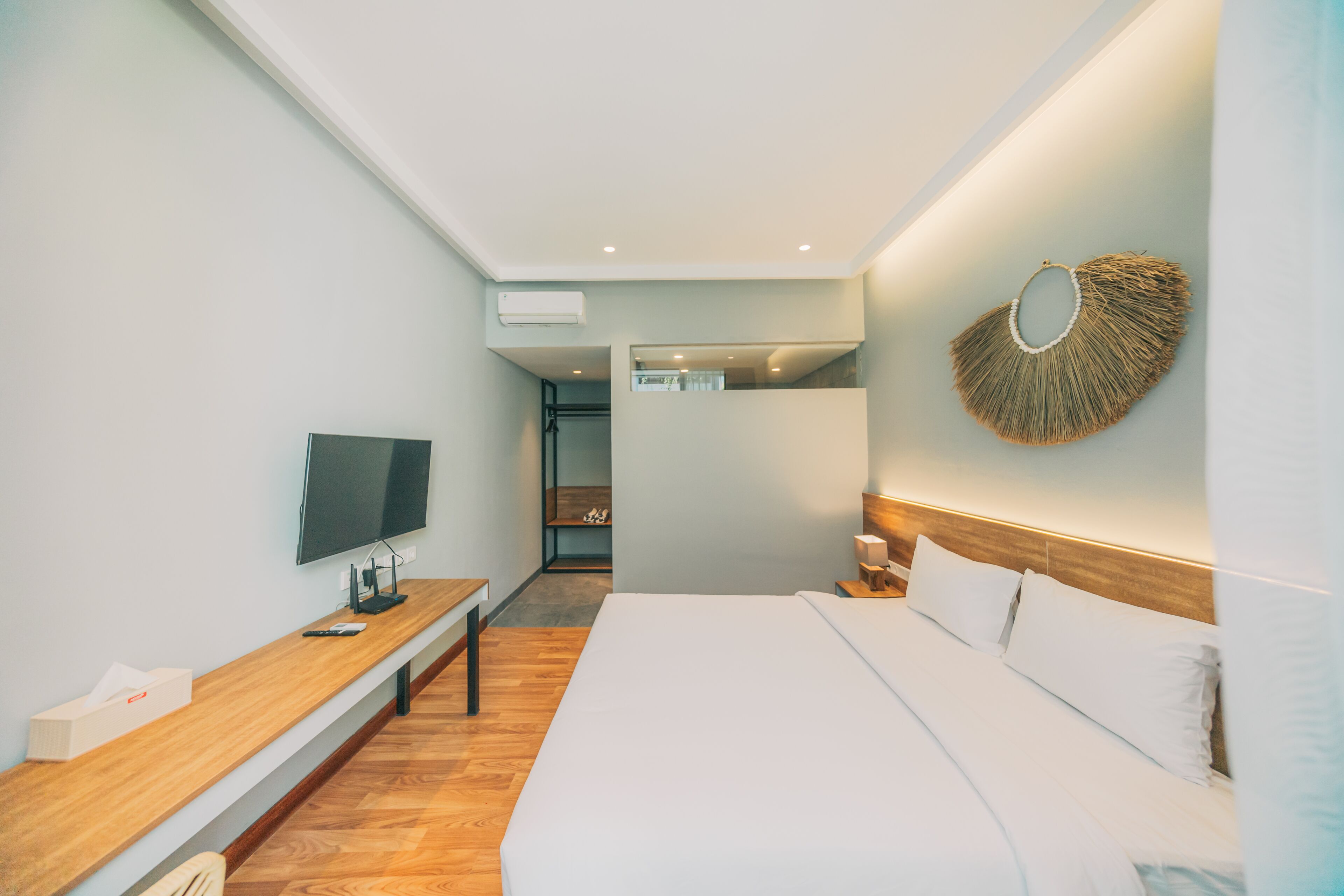 Habitació d'hotel moderna amb un llit gran, televisió de pantalla plana, una banca de fusta i un objecte decoratiu penjat a la paret.
