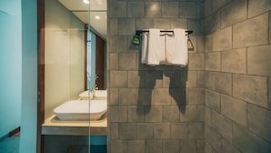 A modern bathroom with a glass partition, a sink, and a towel rack. - Bestah Coliving (Denpasar)