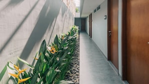 A corridor with a row of doors on one side and a wall with vertical slats on the other. - Bestah Coliving (Denpasar)