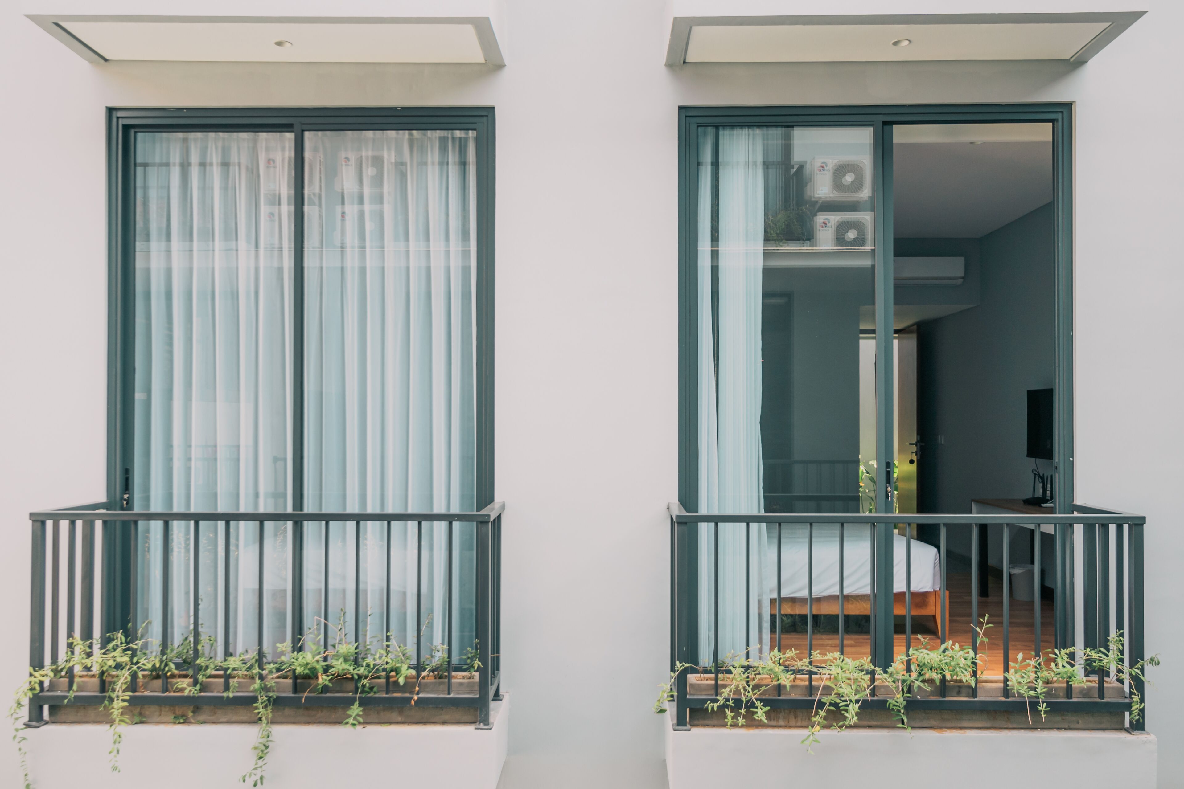 Dos balcones con barandillas de metal y macetas con plantas.