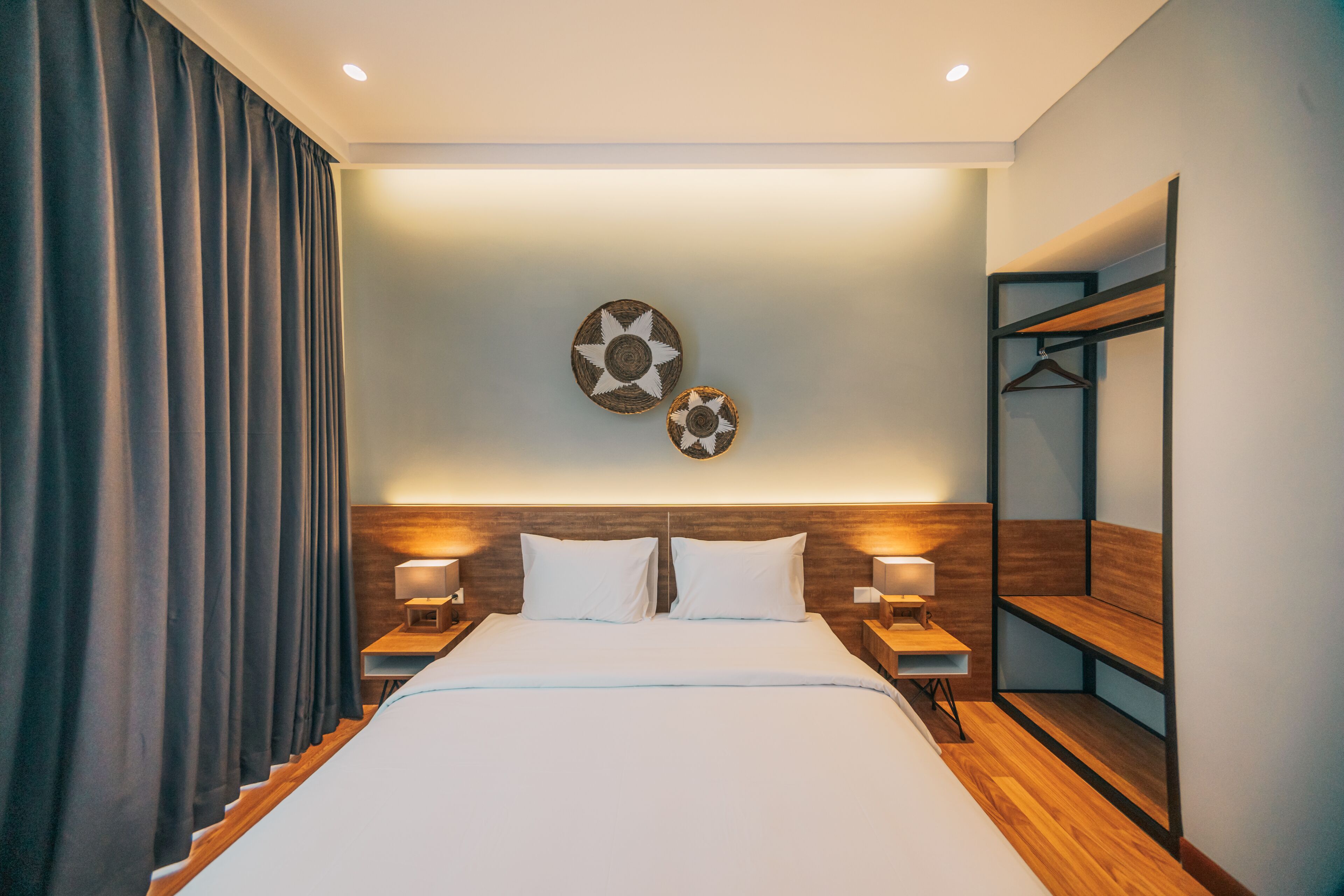 A modern hotel room with a large bed, wooden headboard, two wall-mounted lamps, and a mirror with shelves.