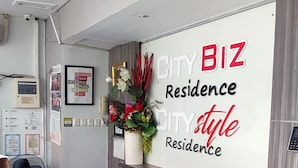 A reception area with a modern design, featuring a reception desk, a wall-mounted sign reading "CITY BIZ Residence," and a decorative plant. - City Style Residence (Jakarta)