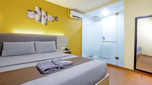 A hotel room with a bed, a bedside table, a wall-mounted air conditioner, and a glass shower enclosure. - City Style Residence (Jakarta)