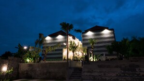 A modern building with a flat roof and horizontal lines, surrounded by palm trees and a concrete wall. - Musa Canggu by Zuzu (Tibubeneng)