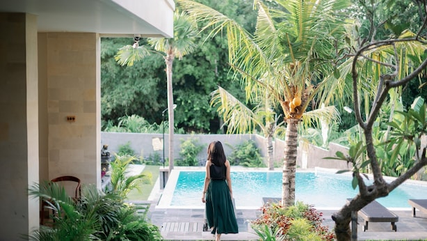 A woman walking towards a pool in a lush garden with palm trees and a clear blue pool. - Musa Canggu by Zuzu (Tibubeneng)