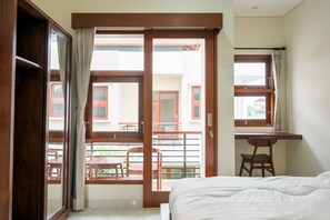 A bedroom with a bed, a desk, and a chair. There is a balcony with a table and chairs. - Musa Canggu by Zuzu (Tibubeneng)
