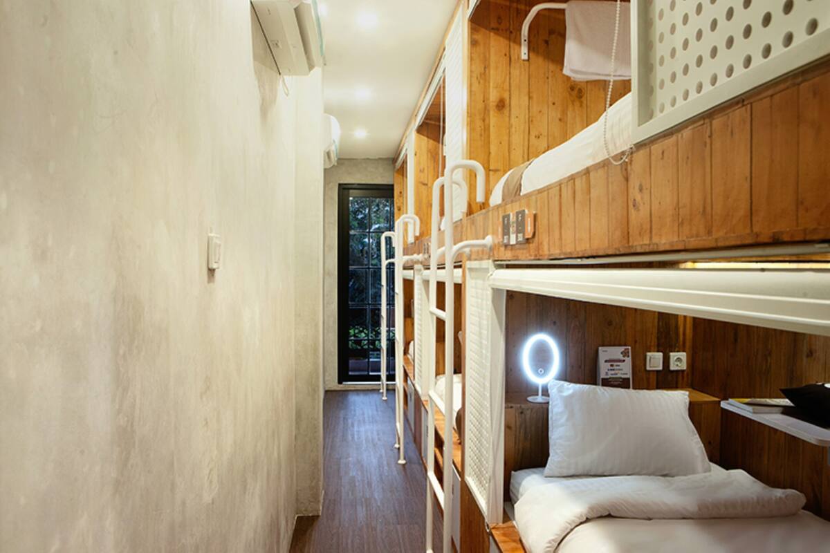 Ein Schlafraum mit Etagenbetten, einer Holzbalkendecke, einem kleinen Nachttisch mit Lampe und Blick ins Freie.