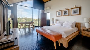 Un dormitorio con una cama grande, un banco de madera, un escritorio y vistas al exterior.