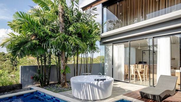 Un área de piscina moderna al aire libre con un jacuzzi, una tumbona y plantas tropicales.