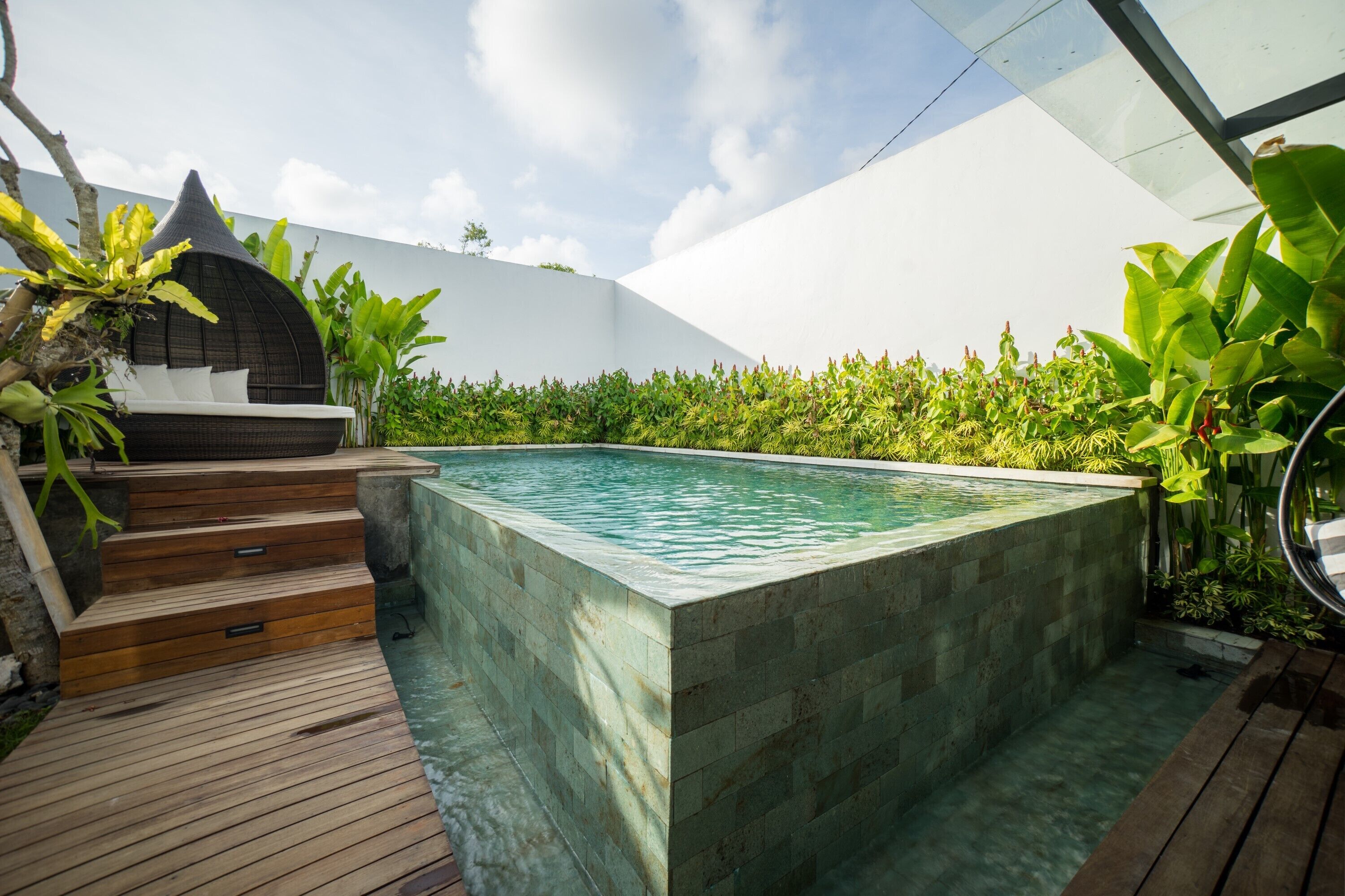 A rectangular pool with a wooden deck and steps leading to a seating area.