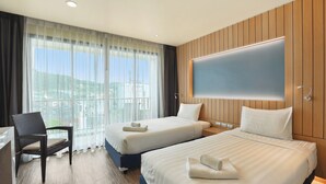 A hotel room with two beds, a desk, a chair, and a large window with curtains. - Dome Kata Resort (Karon)