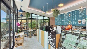 A modern cafe interior with a counter, menu boards, and seating area. - Dome Kata Resort (Karon)