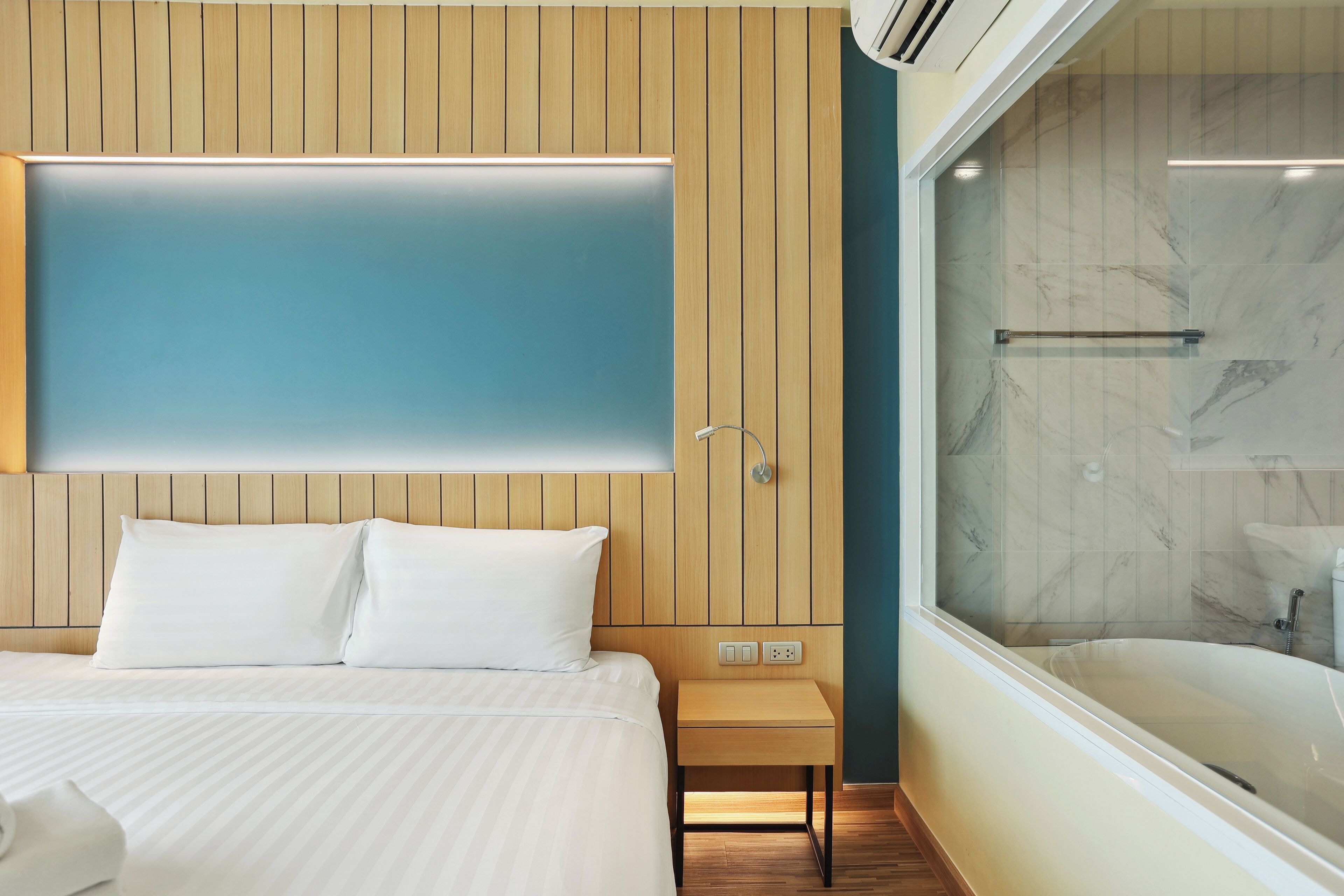A hotel room with a bed, a nightstand, a wall-mounted TV, and a bathroom with a bathtub and shower.