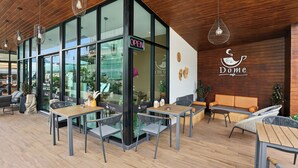 A cafe interior with tables and chairs, a wooden ceiling, and a glass wall. - Dome Kata Resort (Karon)
