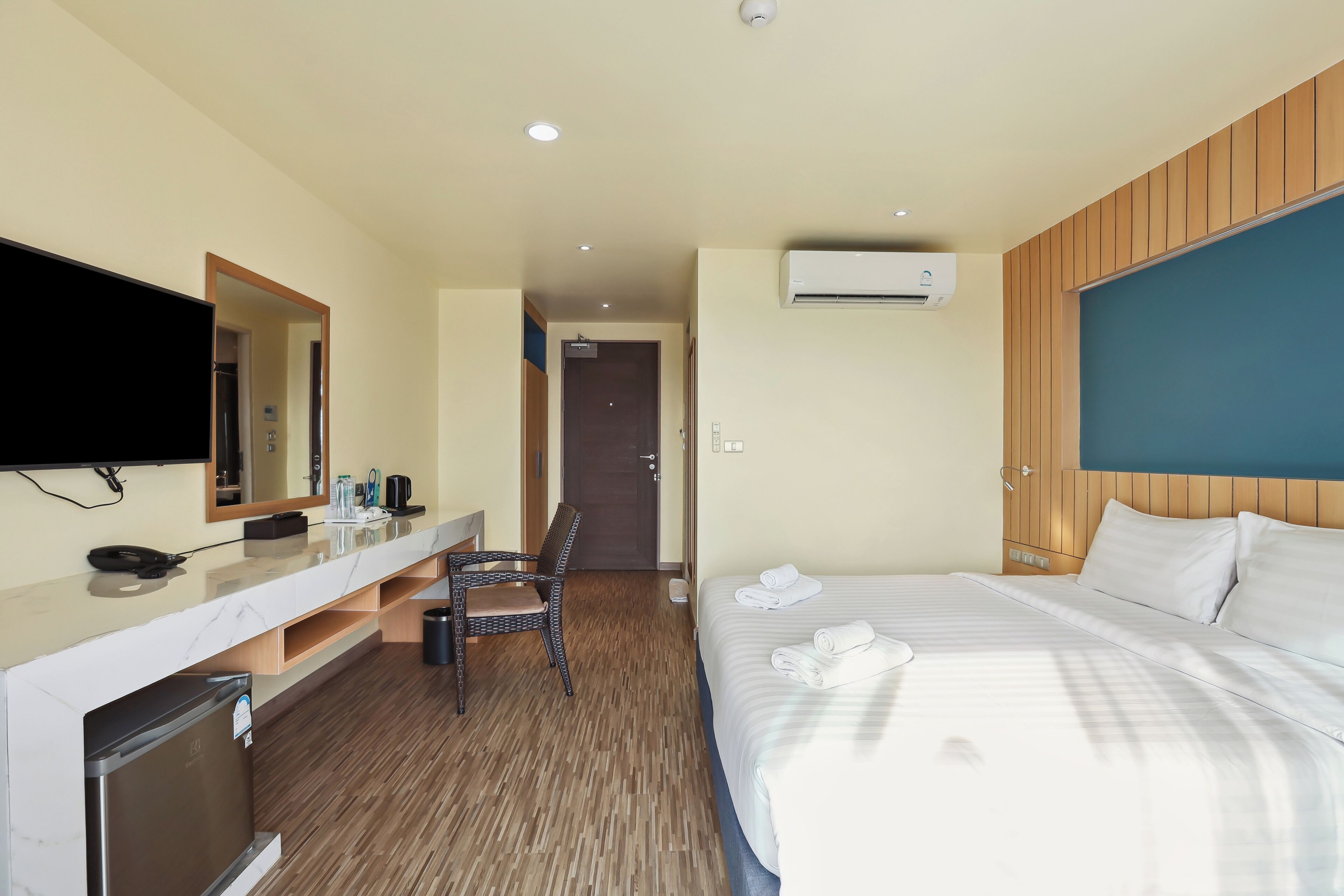 A hotel room with a bed, a desk with a mirror, a television, and an air conditioning unit.