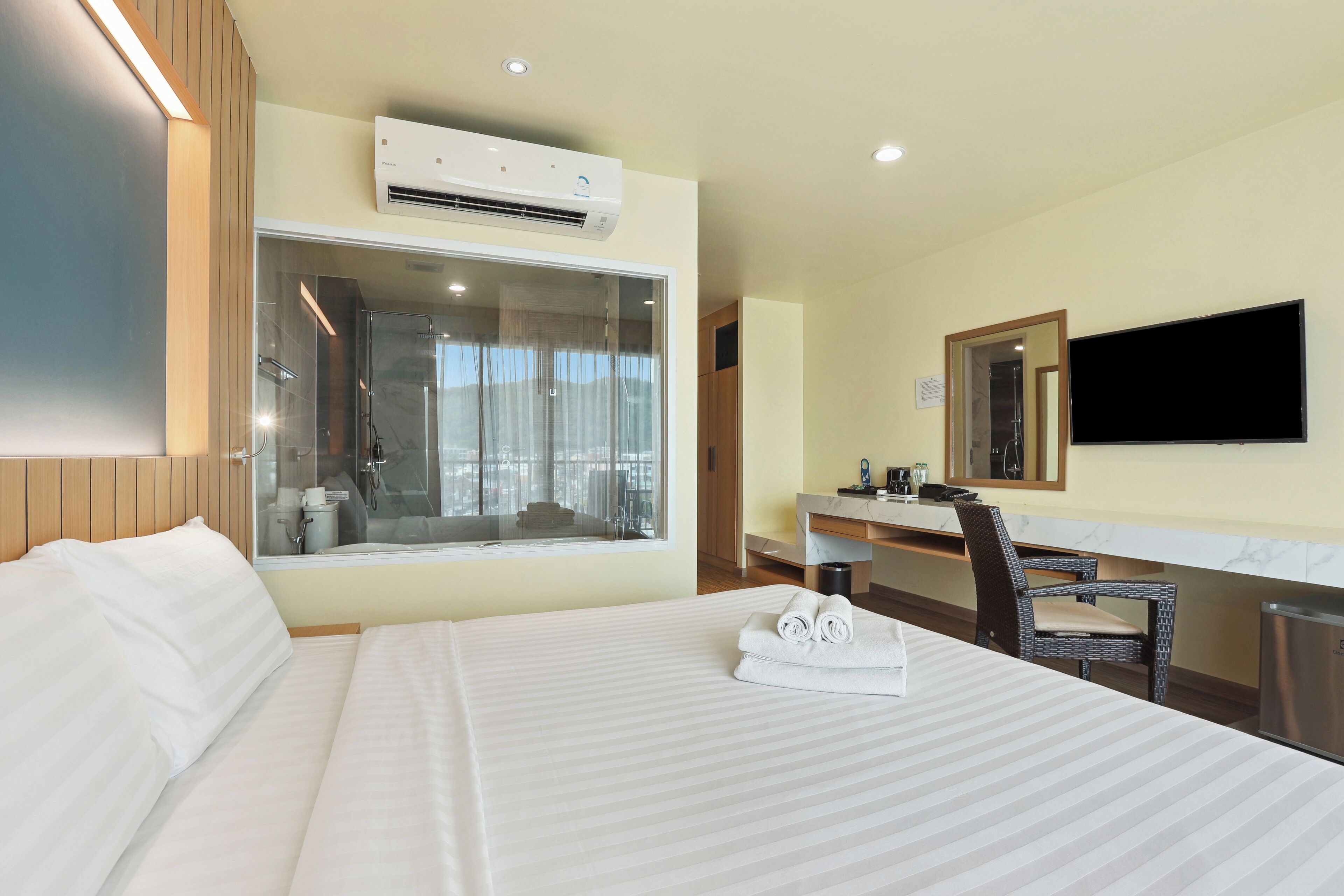 A hotel room with a large bed, a bathroom with a glass shower, a desk with a chair, and a flat-screen TV mounted on the wall.