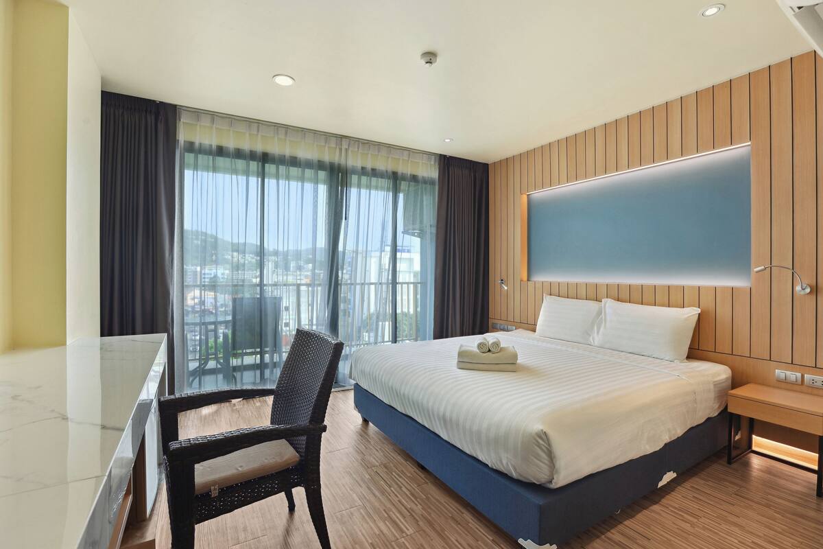 Habitación de hotel con una cama grande, un escritorio, una silla y un televisor en la pared.