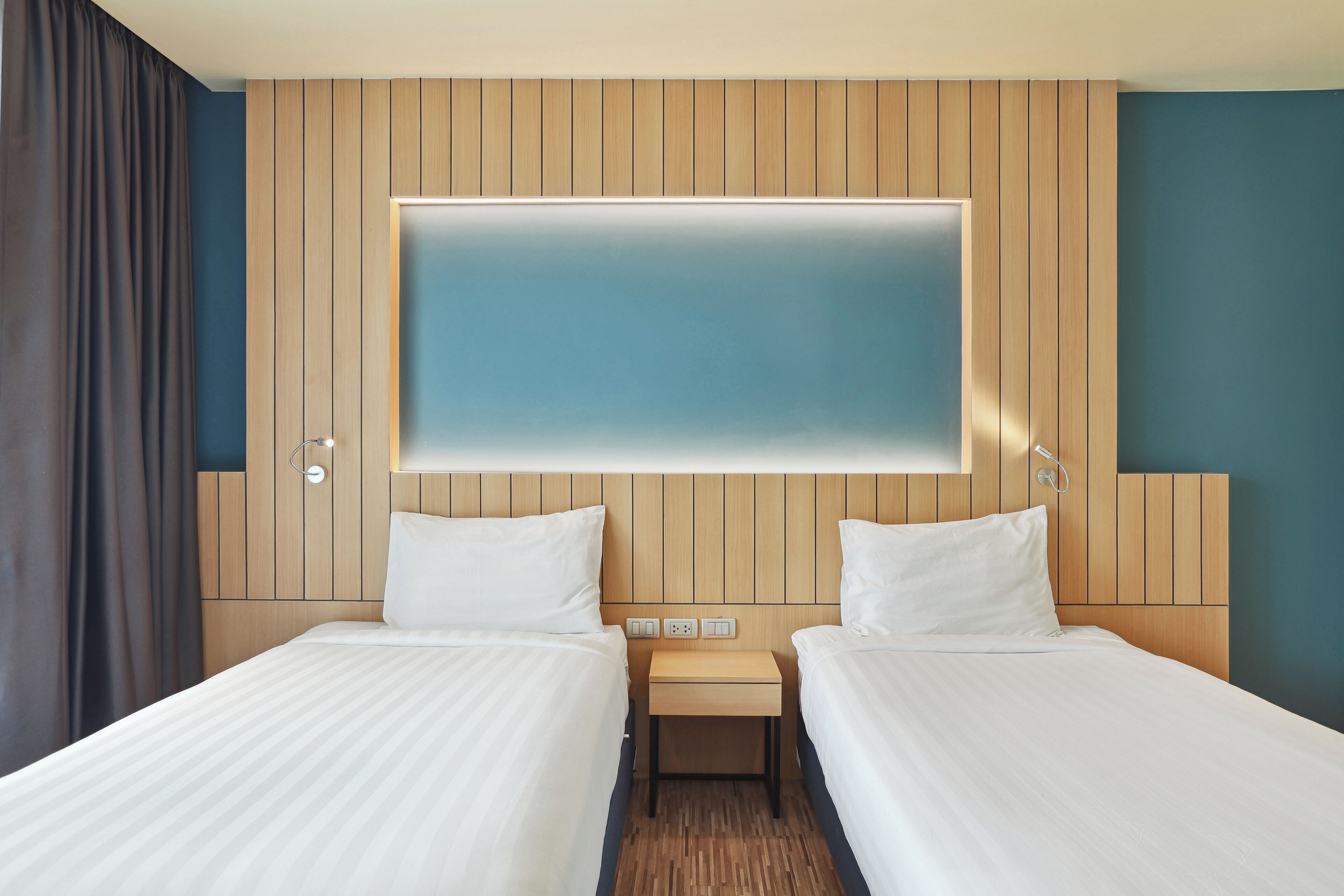 A hotel room with two beds, a wooden headboard, a flat-screen TV, and a small bedside table.