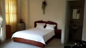 A bedroom with a wooden bed, white bedding, a nightstand, a wall-mounted plant, and a bathroom visible through an open door. - Gianni 2 Hotel (Ho Chi Minh City)