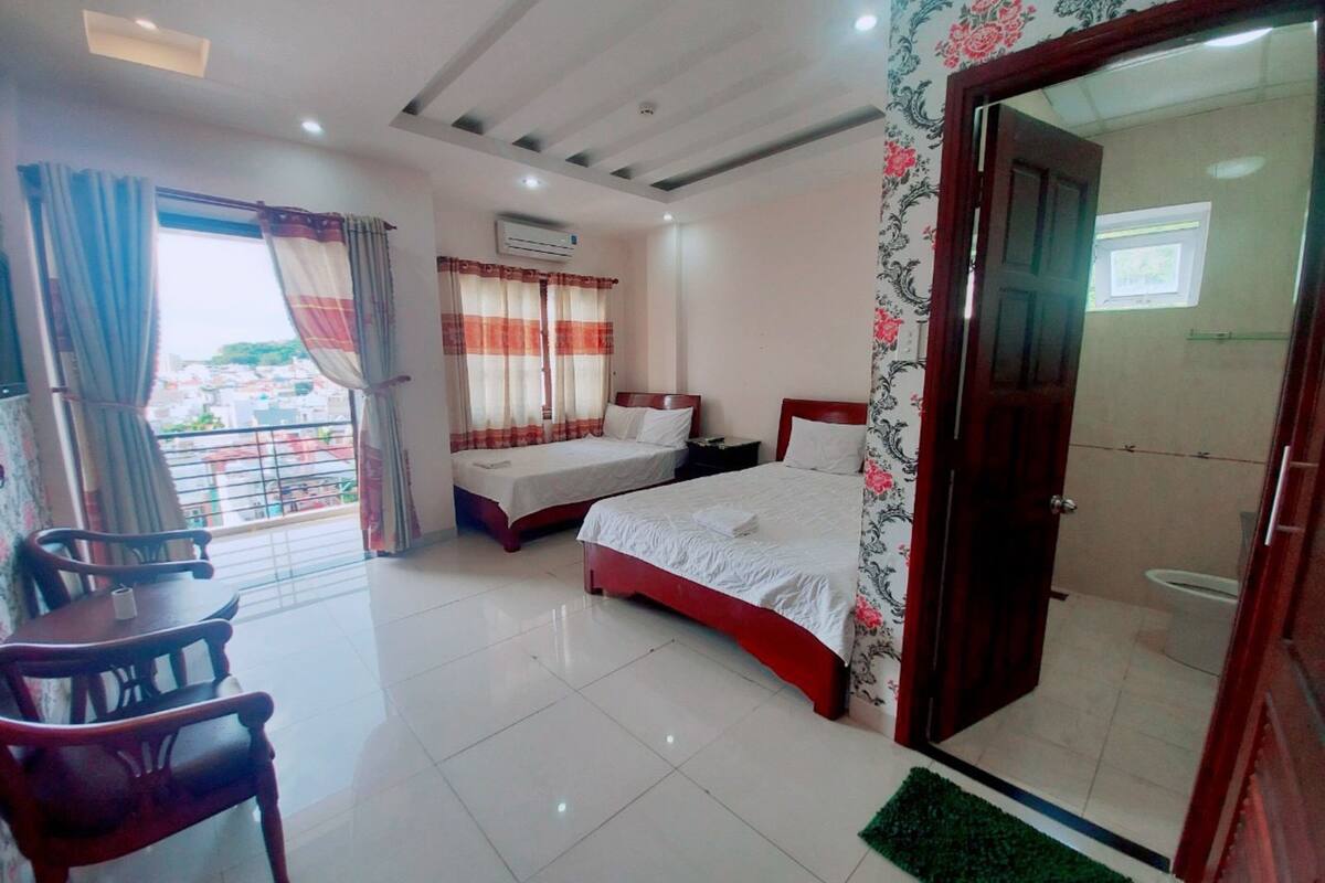 A hotel room with two beds, a balcony, a desk, and a bathroom.
