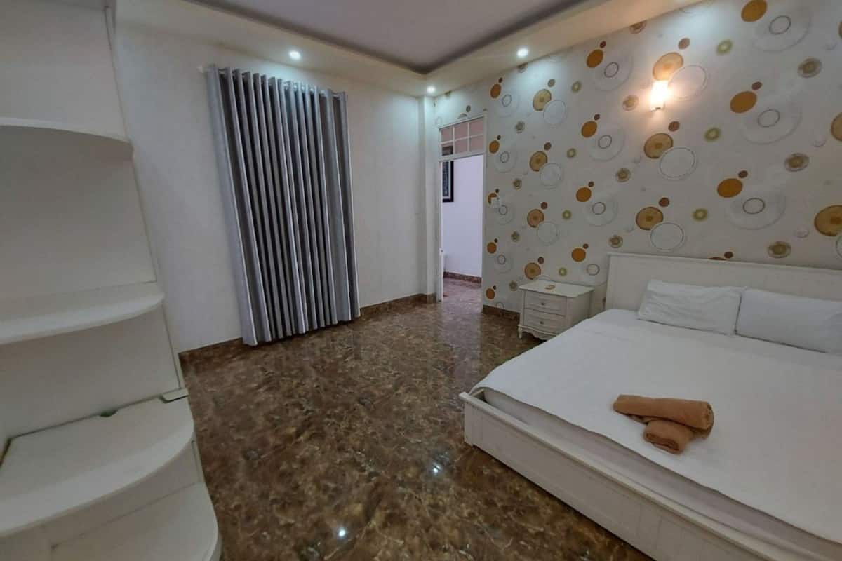 A modern hotel room with a large bed, a white wardrobe, a bathroom with a shower, and a patterned wall.
