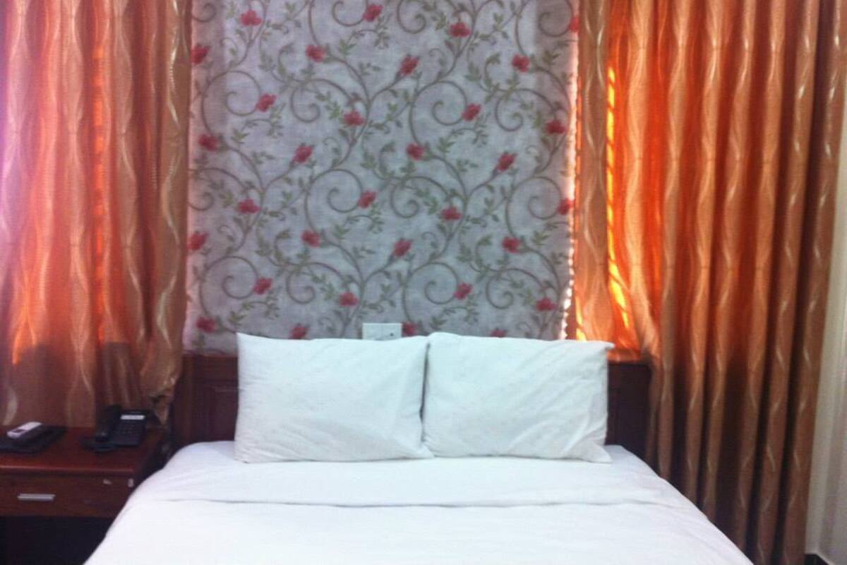 Een hotelkamer met een bed, twee kussens, een nachtkastje, een telefoon en gordijnen.
