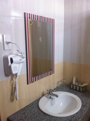 Een badkamer met een witte wastafel, een spiegel met een gestreepte lijst, een haardroger en een klein glazen potje.