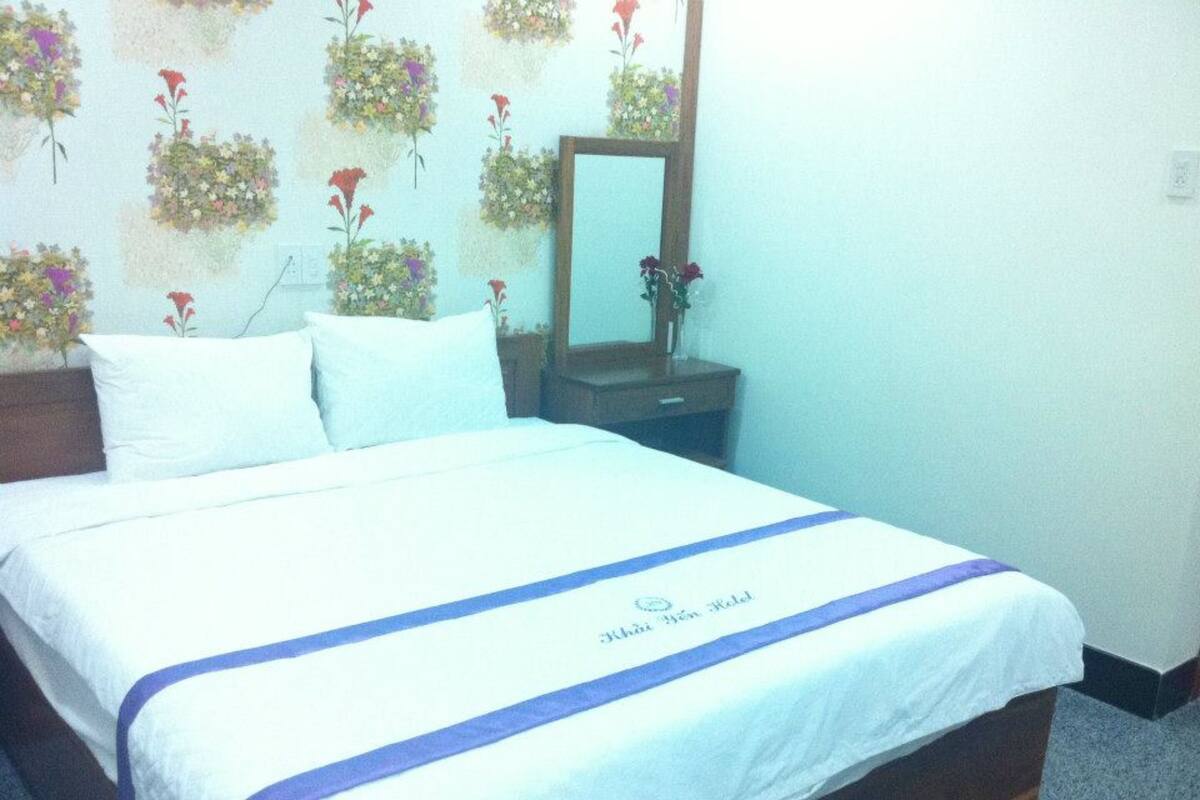 Een hotelkamer met een bed, kussens, een nachtkastje, een spiegel en bloemenbehang.