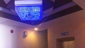 Un ascenseur avec une plaque indiquant « TANG 3 » et un panneau de commande doté d’un voyant rouge.