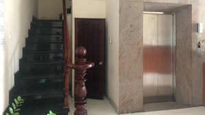 A staircase with a wooden handrail leading to a door, an elevator, and a marble wall.