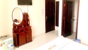 A hotel room with a wooden dresser, a flat-screen TV mounted on the wall, a mirror, a small refrigerator, and a bed with a white bedspread.