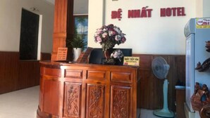 A reception desk with a wooden design, a clock wall, and a sign for the De Nhat Hotel.