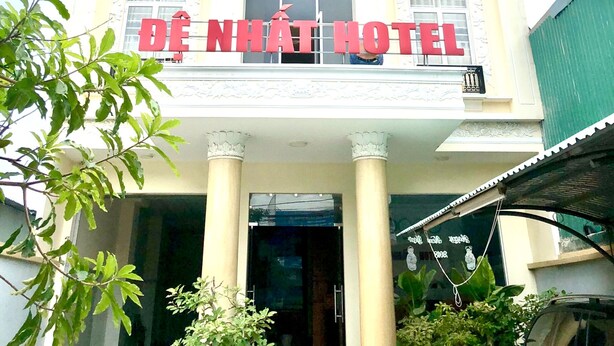 A hotel building with a large central window, multiple balconies, and a prominent sign reading "DE NHAT HOTEL".