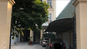 Un letrero de bienvenida en la entrada del Khách Sạn Định Nhat, con una zona de estacionamiento techada y dos coches aparcados en su interior.
